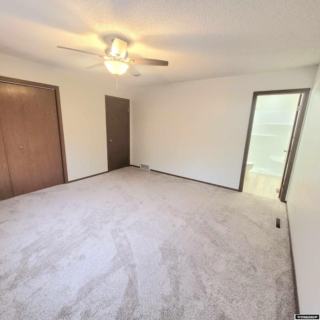 unfurnished bedroom with ensuite bathroom, a textured ceiling, ceiling fan, carpet floors, and a closet