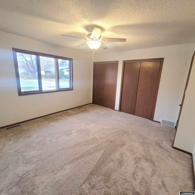 unfurnished bedroom with a textured ceiling, ceiling fan, light carpet, and multiple closets