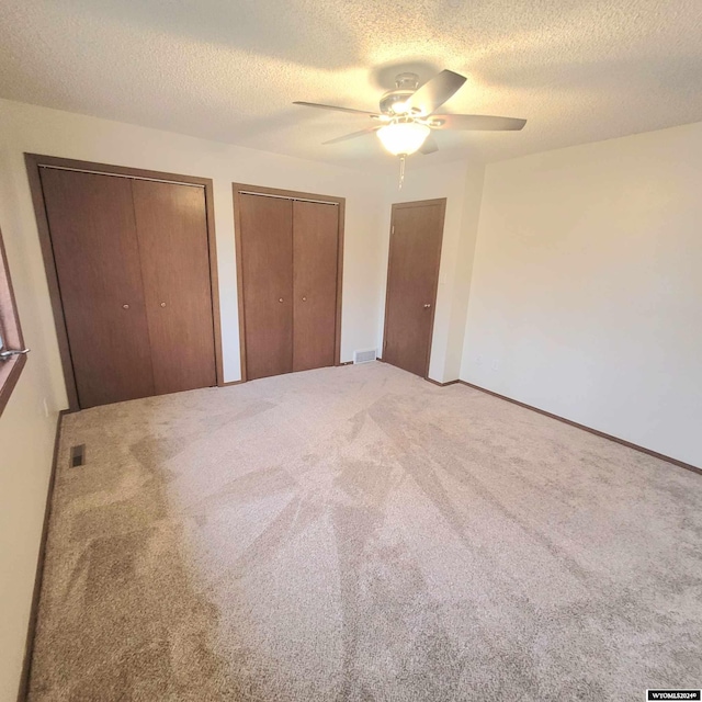 unfurnished bedroom with carpet, ceiling fan, a textured ceiling, and multiple closets