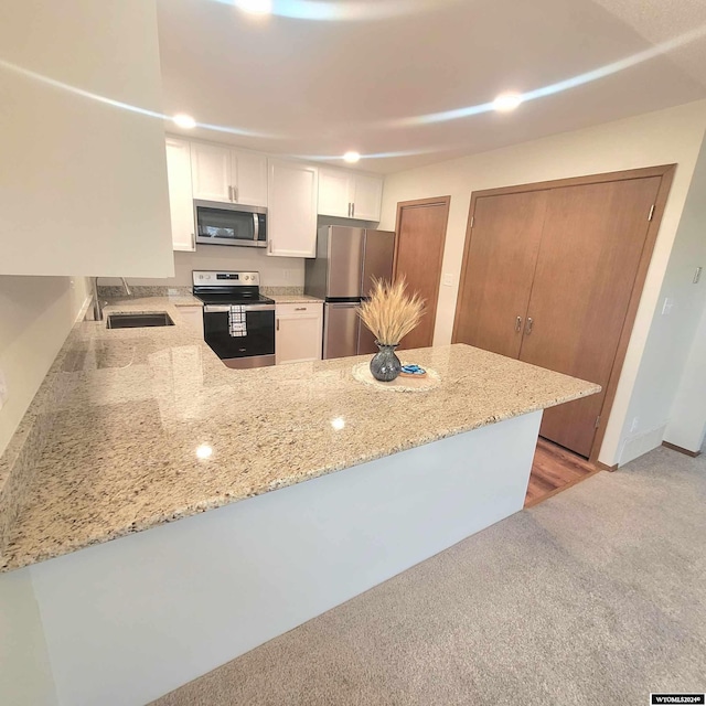 kitchen with white cabinets, sink, light stone counters, kitchen peninsula, and stainless steel appliances