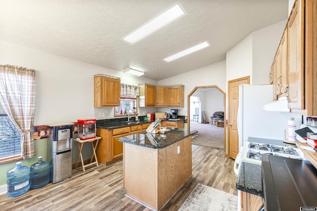 kitchen with lofted ceiling, dark stone countertops, a kitchen island, a textured ceiling, and light hardwood / wood-style floors