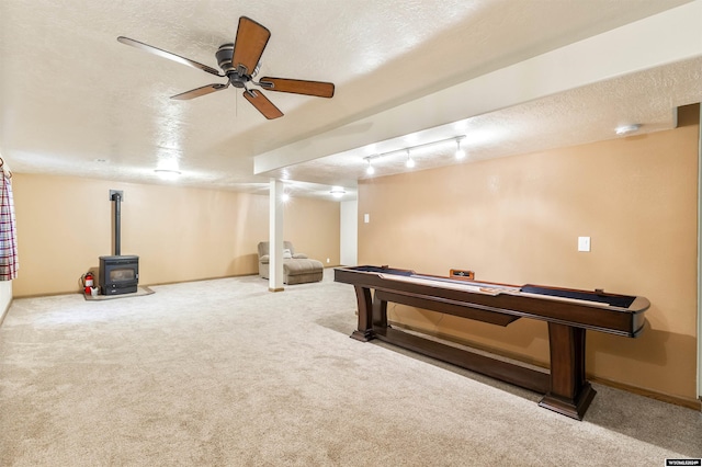 game room with carpet, a textured ceiling, a wood stove, and ceiling fan