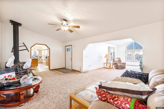 living room featuring a wood stove, ceiling fan, carpet floors, a textured ceiling, and lofted ceiling