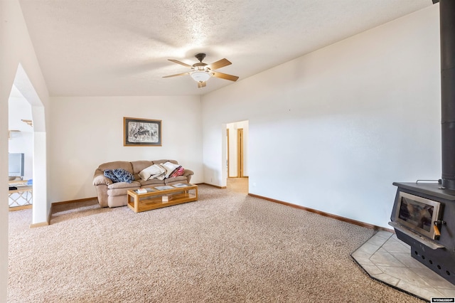 carpeted living room featuring a textured ceiling, a wood stove, ceiling fan, and lofted ceiling