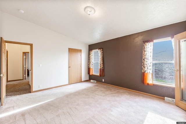 unfurnished room with a textured ceiling, light carpet, and lofted ceiling