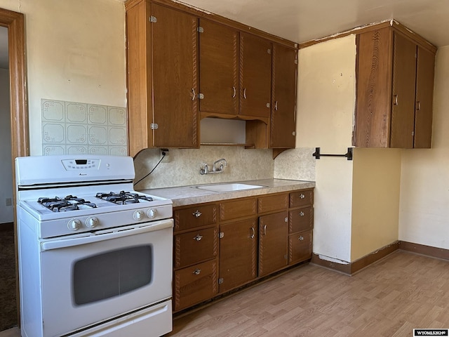 kitchen featuring backsplash, white gas stove, light hardwood / wood-style floors, and sink