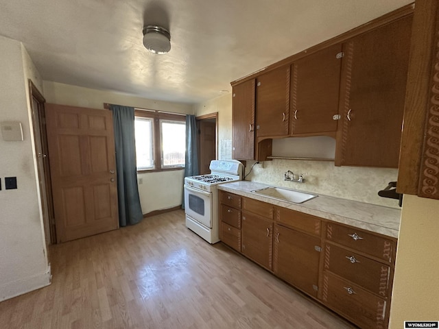 kitchen featuring white range with gas stovetop, light wood-type flooring, backsplash, and sink