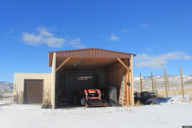 snow covered structure featuring a carport, a mountain view, and a garage