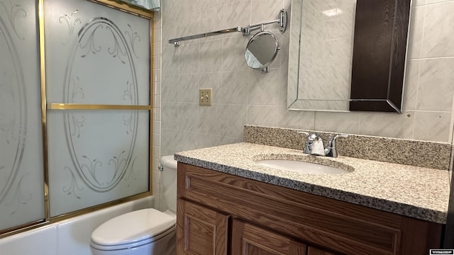 full bathroom featuring combined bath / shower with glass door, toilet, tile walls, and vanity