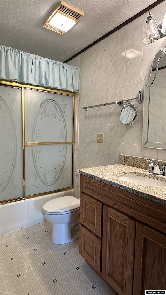 full bathroom featuring combined bath / shower with glass door, a textured ceiling, toilet, vanity, and tile walls