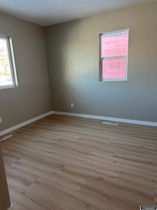 empty room with a textured ceiling and light hardwood / wood-style flooring