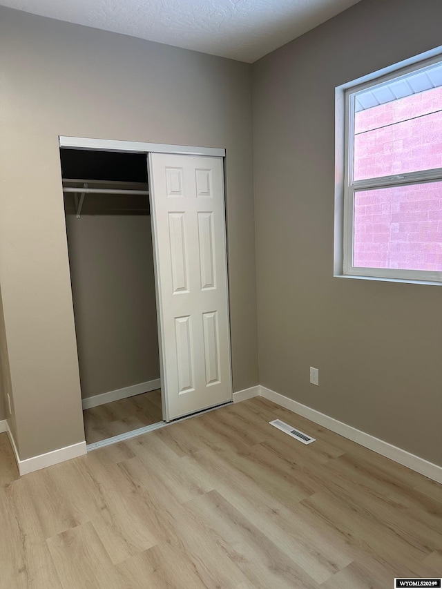 unfurnished bedroom with light wood-type flooring, a textured ceiling, and a closet