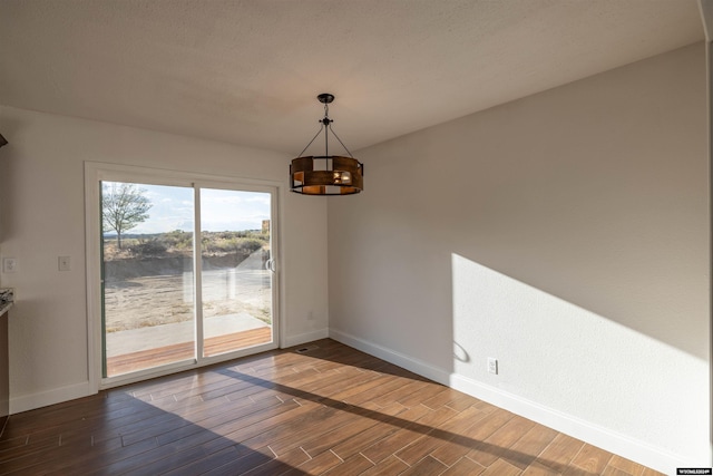 unfurnished dining area featuring dark hardwood / wood-style flooring, a textured ceiling, and a chandelier