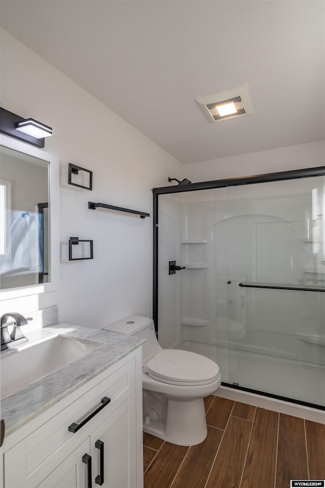 bathroom featuring wood-type flooring, vanity, toilet, and a shower with door