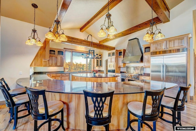 kitchen featuring a kitchen bar, wall chimney exhaust hood, built in appliances, vaulted ceiling with beams, and light hardwood / wood-style floors