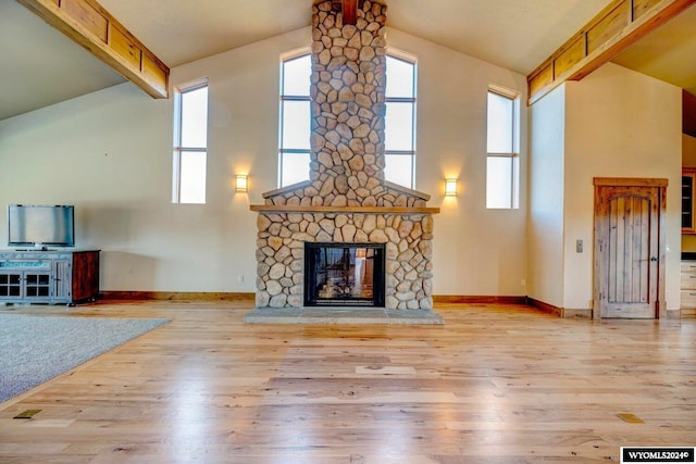 unfurnished living room with lofted ceiling with beams, light hardwood / wood-style flooring, a healthy amount of sunlight, and a stone fireplace