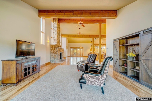 living room with a stone fireplace, a wealth of natural light, ceiling fan, and light wood-type flooring