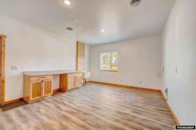 unfurnished living room featuring built in desk and light wood-type flooring