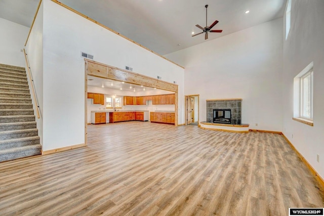 unfurnished living room with a fireplace, light hardwood / wood-style flooring, high vaulted ceiling, and ceiling fan