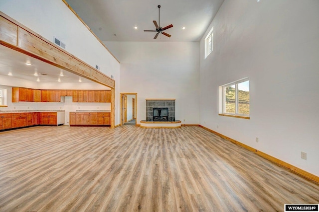 unfurnished living room featuring a fireplace, a towering ceiling, light hardwood / wood-style flooring, and ceiling fan