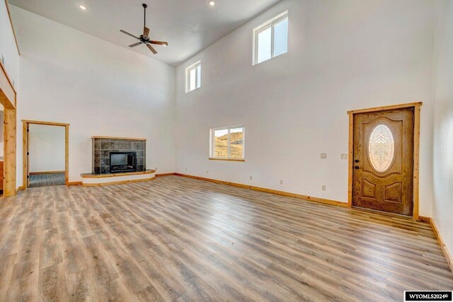 unfurnished living room with ceiling fan, light hardwood / wood-style floors, a tile fireplace, and high vaulted ceiling