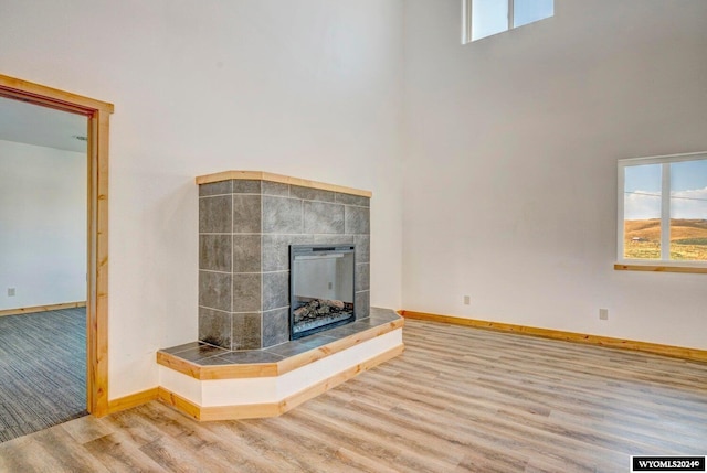 unfurnished living room featuring hardwood / wood-style flooring, a high ceiling, and a tile fireplace