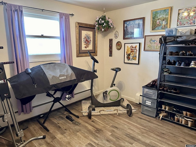 exercise room with wood-type flooring and a baseboard heating unit