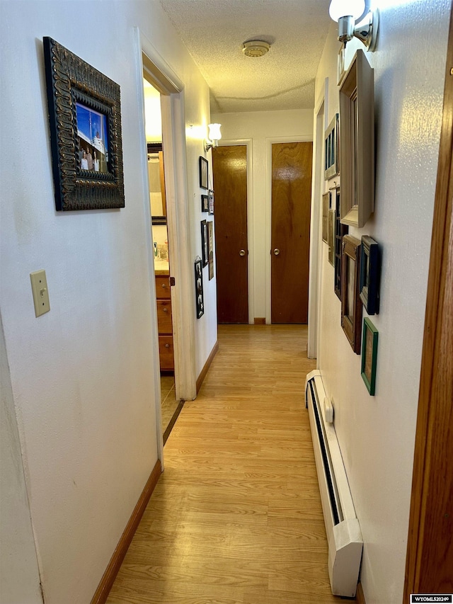 hallway with light hardwood / wood-style floors, a textured ceiling, and a baseboard heating unit