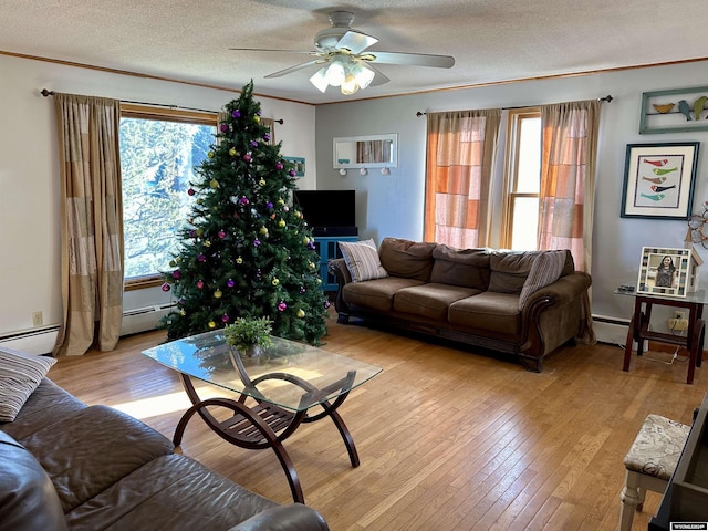 living room with a baseboard heating unit, ceiling fan, ornamental molding, light wood-type flooring, and a textured ceiling