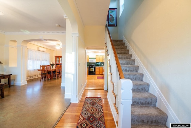 stairs featuring a wall mounted air conditioner, ceiling fan, wood-type flooring, and crown molding