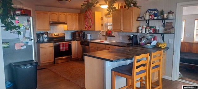 kitchen featuring light brown cabinetry, sink, kitchen peninsula, a breakfast bar, and stainless steel appliances