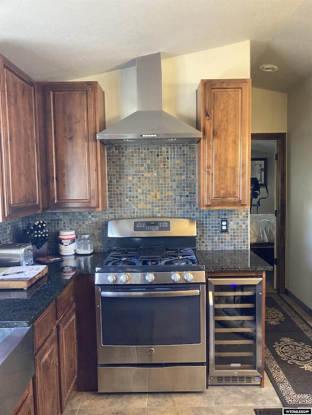 kitchen featuring dark stone counters, wine cooler, wall chimney exhaust hood, decorative backsplash, and gas stove