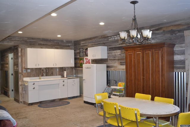 kitchen featuring wooden walls, decorative light fixtures, white fridge, white cabinetry, and a chandelier