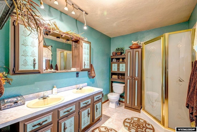 bathroom with vanity, toilet, a shower with shower door, and a textured ceiling