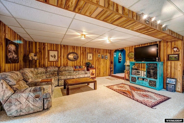 carpeted living room featuring a drop ceiling and wood walls