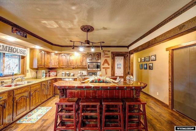 kitchen with ornamental molding, sink, dark hardwood / wood-style floors, a kitchen island, and stainless steel microwave