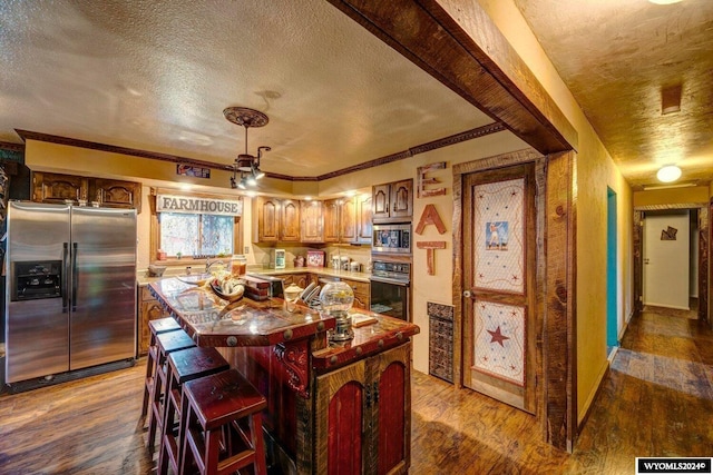 kitchen featuring a center island, stainless steel appliances, a textured ceiling, hardwood / wood-style flooring, and ornamental molding