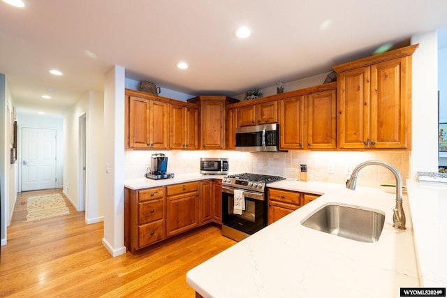 kitchen with sink, light stone counters, backsplash, light hardwood / wood-style floors, and appliances with stainless steel finishes