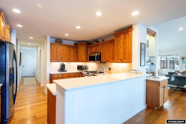 kitchen with sink, kitchen peninsula, decorative backsplash, appliances with stainless steel finishes, and light wood-type flooring