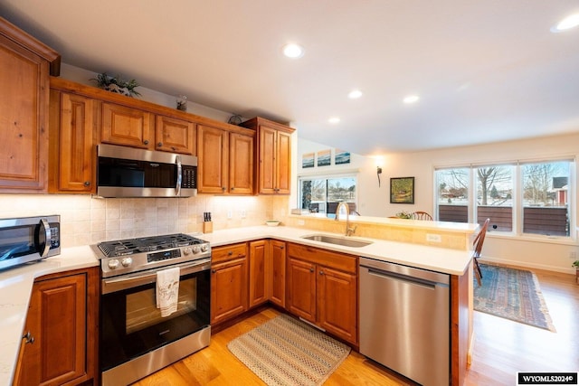 kitchen with sink, stainless steel appliances, backsplash, kitchen peninsula, and light wood-type flooring