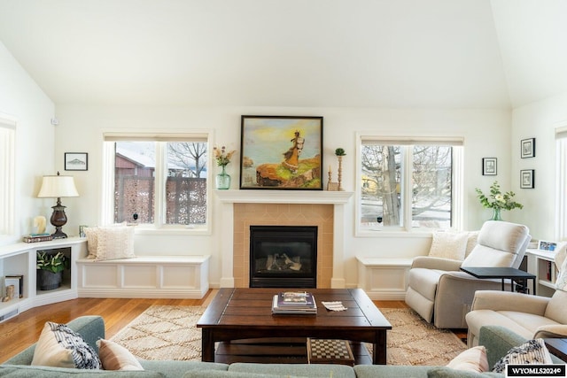 living room with a tile fireplace, light hardwood / wood-style flooring, and lofted ceiling