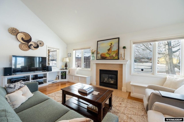 living room featuring a tiled fireplace, high vaulted ceiling, and light hardwood / wood-style floors