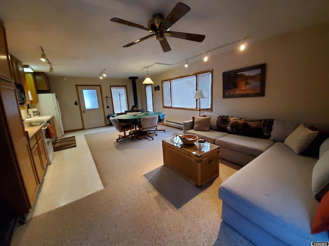 living room featuring a wood stove, ceiling fan, and a baseboard heating unit