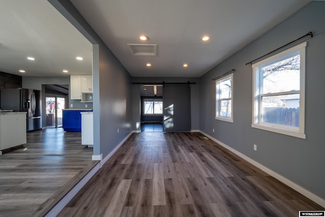 unfurnished living room featuring a barn door, dark hardwood / wood-style flooring, a healthy amount of sunlight, and a baseboard heating unit