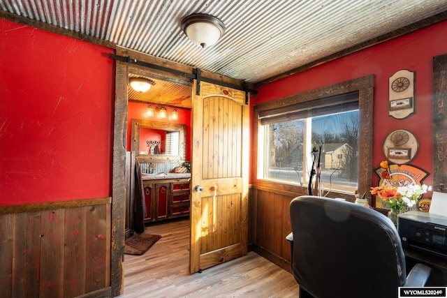 office space with a barn door, wood walls, and light wood-type flooring