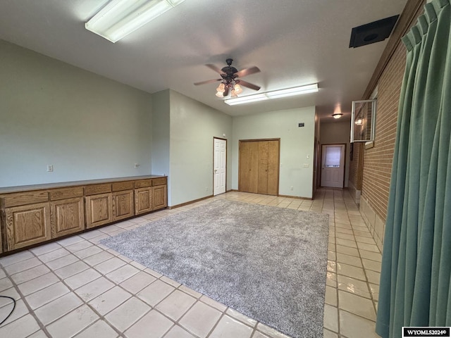 empty room with light tile patterned floors, ceiling fan, and brick wall