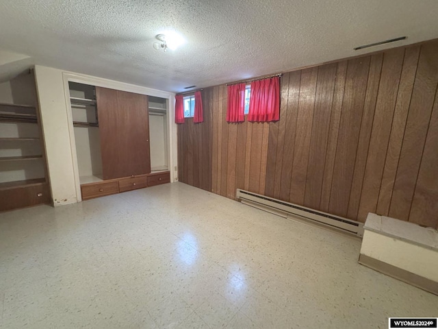 below grade area featuring wood walls, baseboard heating, a textured ceiling, and tile patterned floors