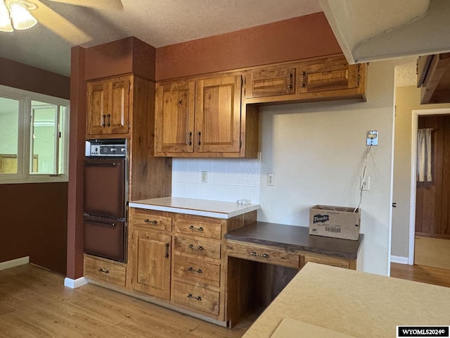 kitchen with light wood-style flooring, oven, a warming drawer, tasteful backsplash, and brown cabinetry