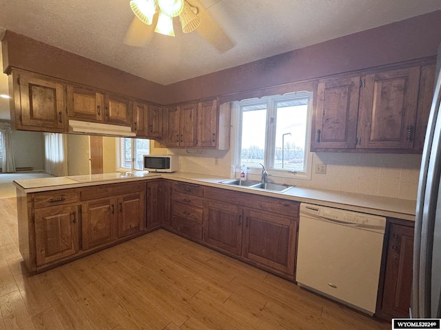 kitchen featuring light wood-type flooring, white dishwasher, a sink, and a peninsula