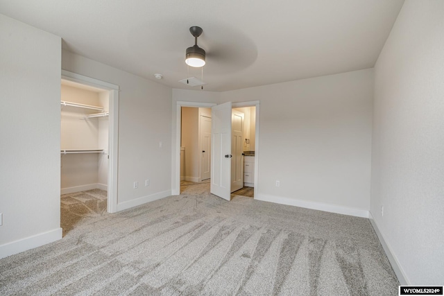 unfurnished bedroom featuring light carpet, a walk in closet, ensuite bathroom, ceiling fan, and a closet